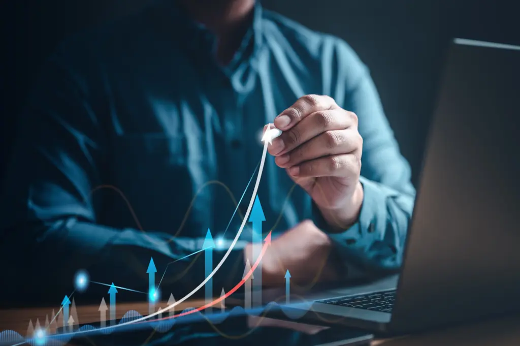 Person in a blue shirt connects a cable beside a laptop, overlaid with upward-trending graphs and arrows in neon colors.